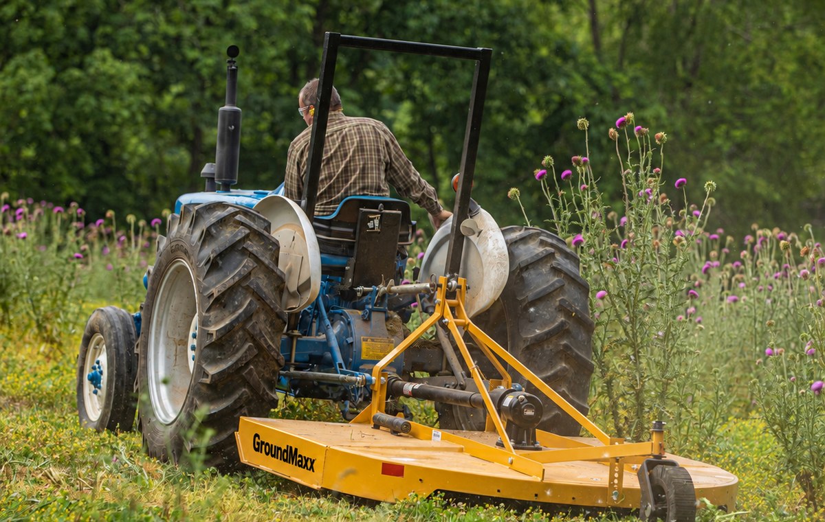 GroundMaxx RC72 rotary cutter mounted on a tractor, cutting a path through a wildflower meadow